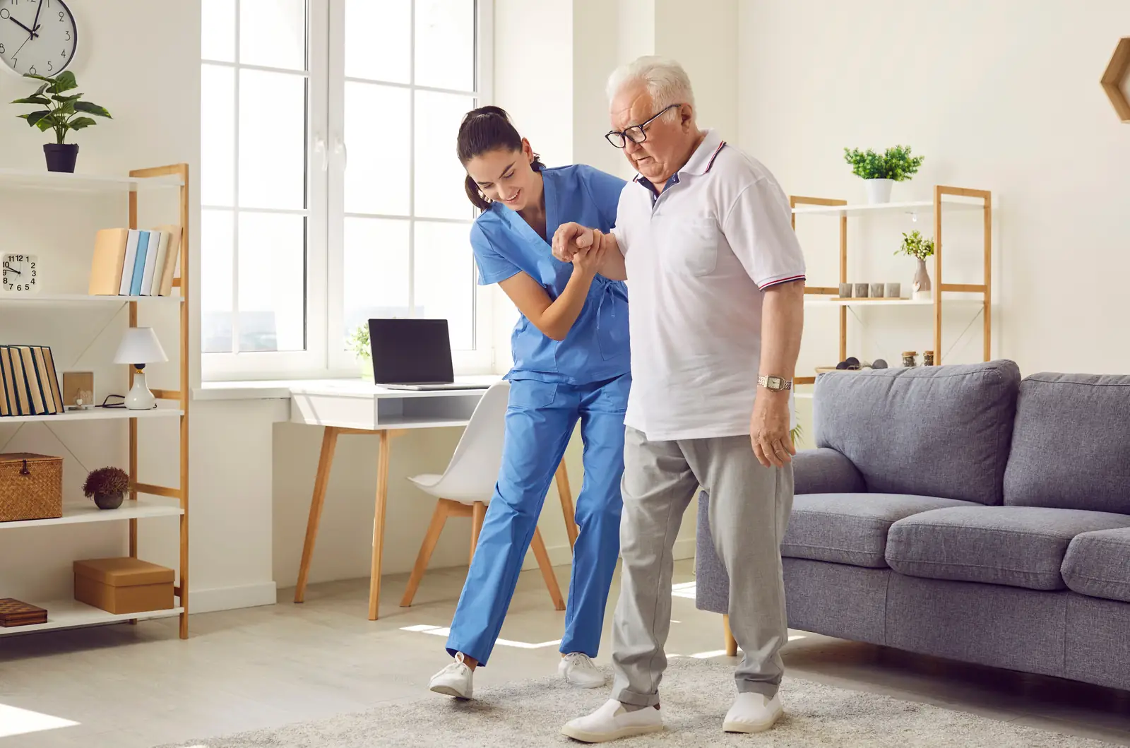 Nurse steadying an older man as he walks across his living room